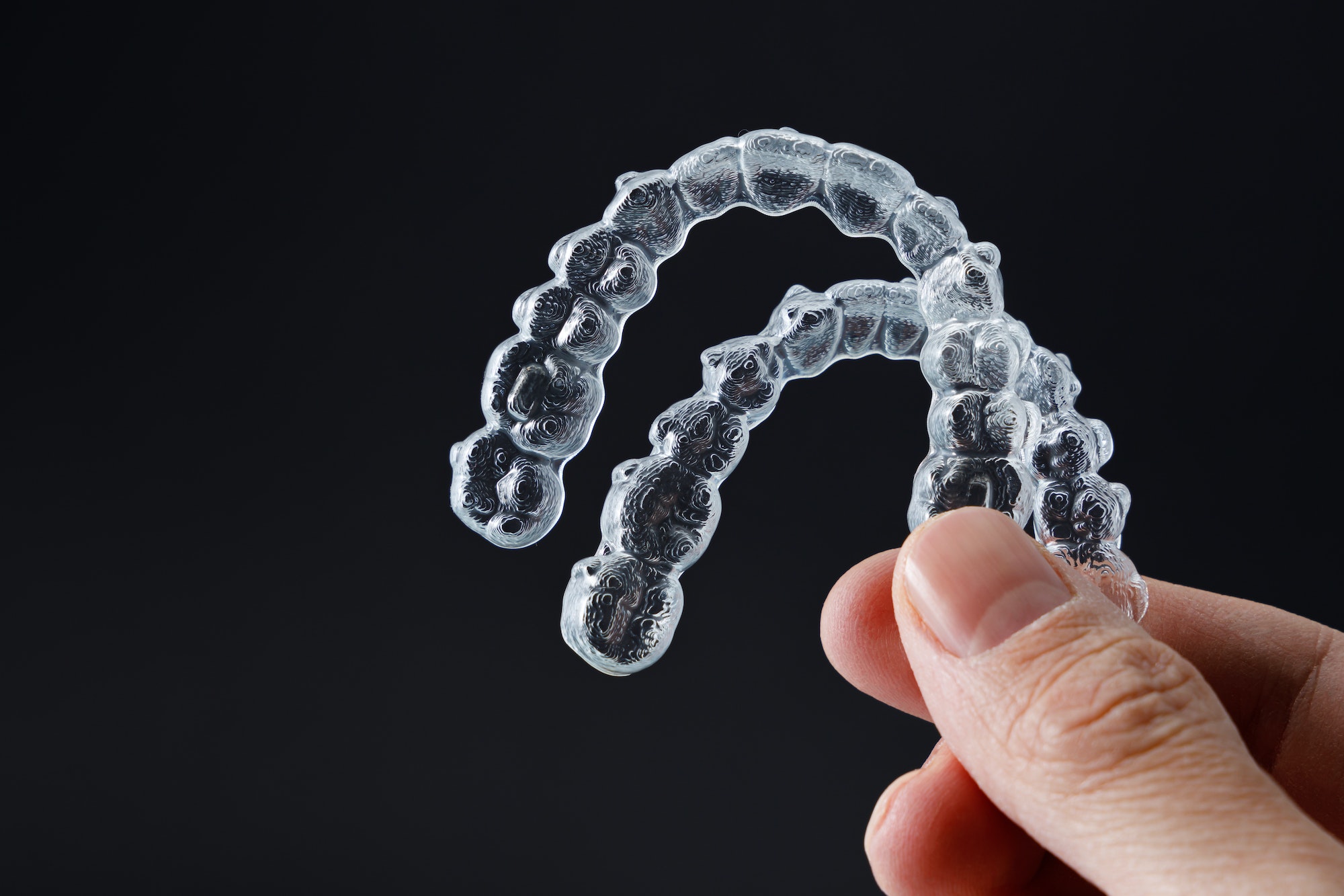 Hand holding two transparent retainers on black background. Invisalign orthodontics concept