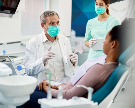 mature-dentist-with-face-mask-talking-to-black-fem-2024-12-13-21-51-55-utc